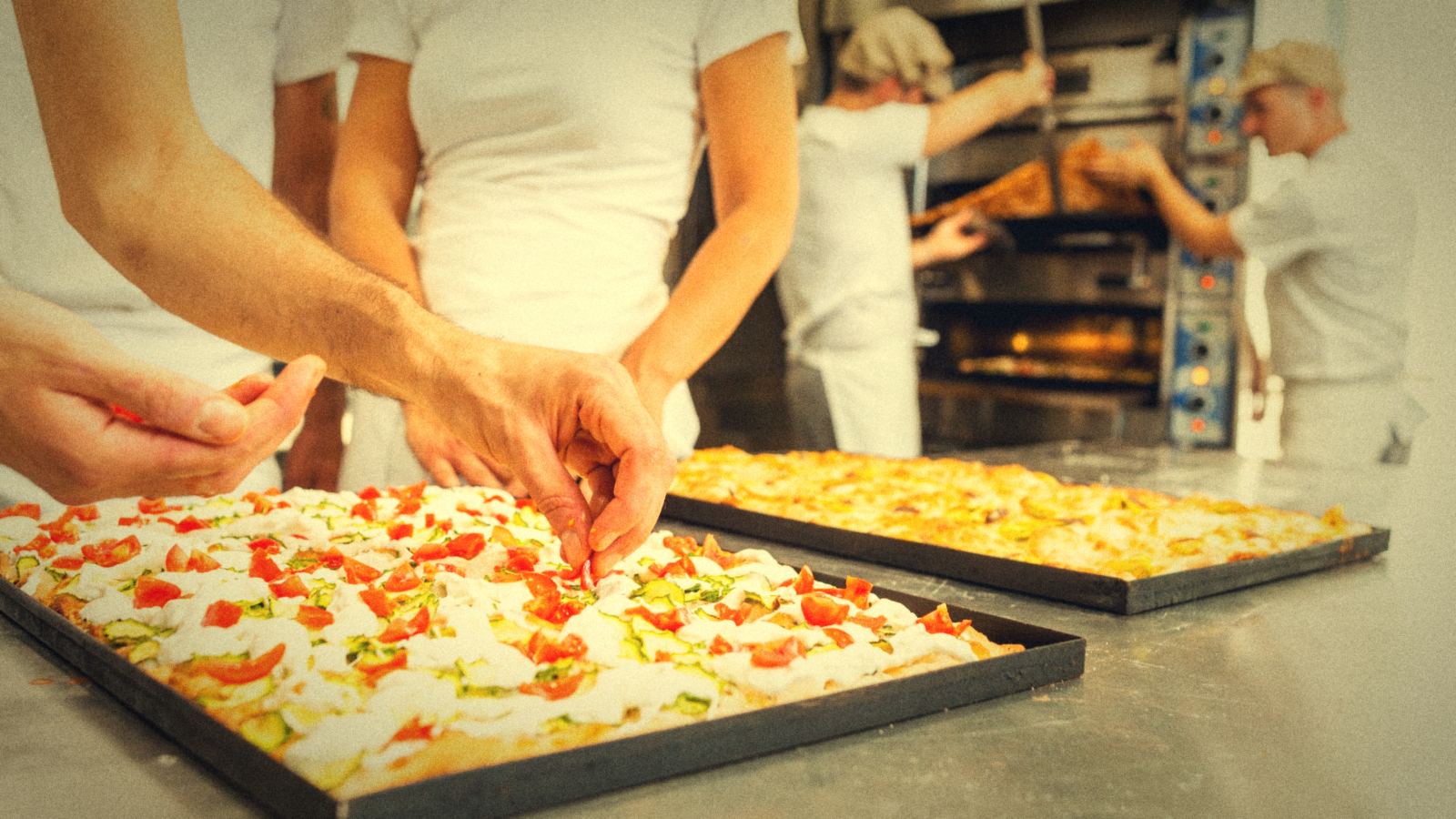 Mani che condiscono una teglia di pizza